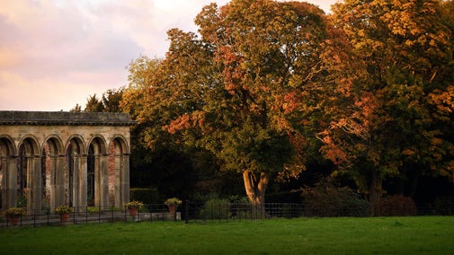 A view of the the stone arches of the Orangery with autumn leaves in the background.
